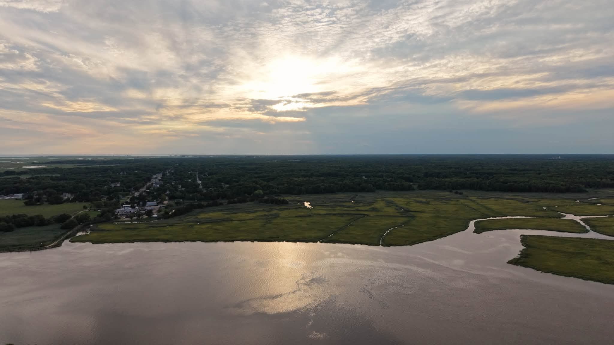 Aerial view of Delaware Bay marshland with sunlight breaking through storm clouds over a small South Jersey village