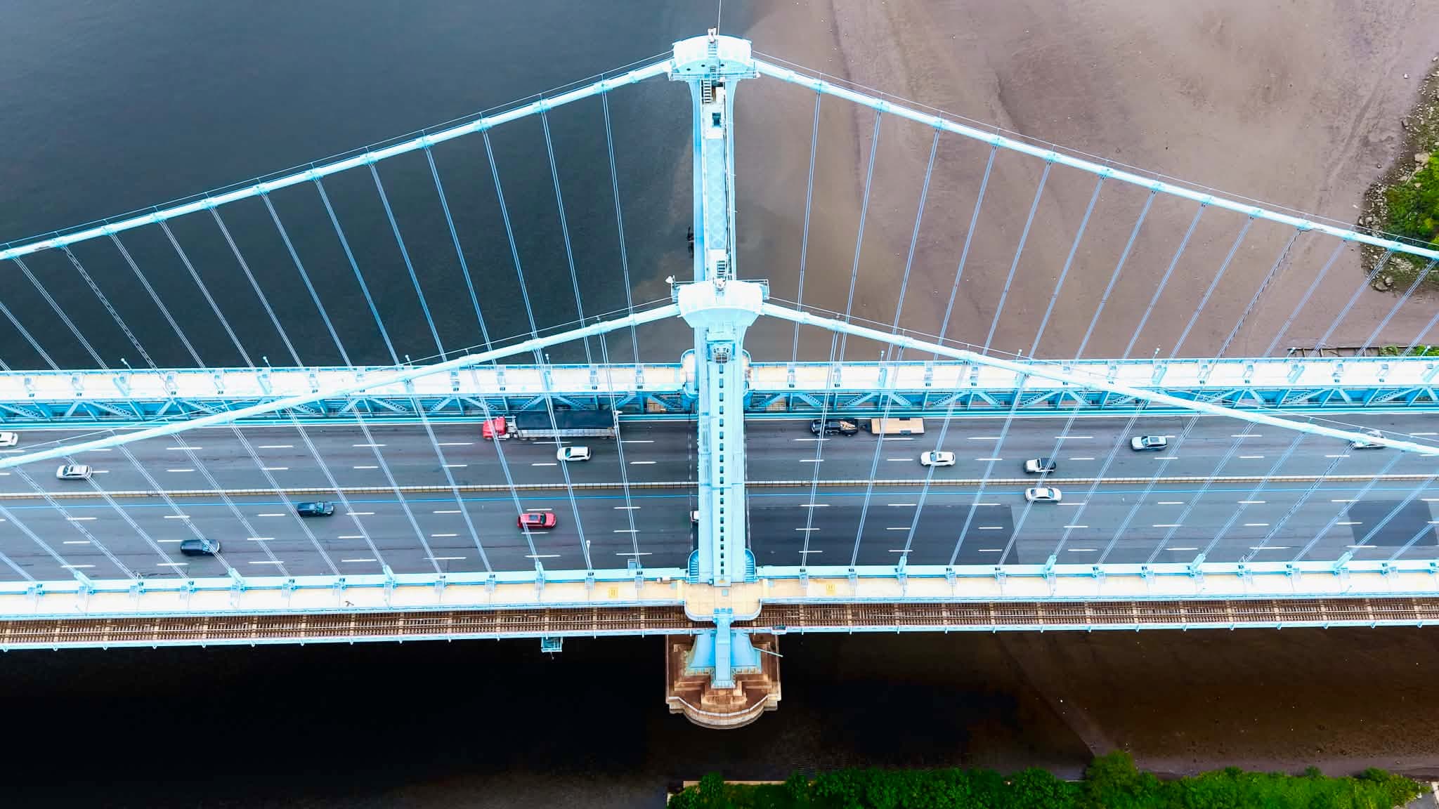 Straight-down aerial photograph of a large bridge crossing water, with traffic lanes, rail tracks, towers, and suspension cables forming a symmetrical geometric pattern
